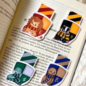 May include: Four colorful bookmarks featuring the Hogwarts house crests with cute animal illustrations. The crests are Gryffindor, Hufflepuff, Slytherin, and Ravenclaw. Each bookmark has a different animal: a lion, a badger, a snake, and an owl.