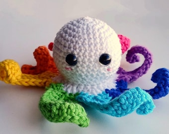 May include: A crocheted octopus toy with a white head and rainbow colored tentacles. The octopus has black eyes and a pink blush on its cheeks.