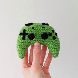 Può includere: Un controller per videogiochi all'uncinetto verde con pulsanti neri.