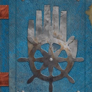 Puede incluir: Una cubierta de libro azul texturizada que presenta una silueta de mano metálica central superpuesta con un timón de barco. Las esquinas están adornadas con emblemas de anclas plateadas y el borde del lomo incluye correas de cuero marrón con remaches plateados.