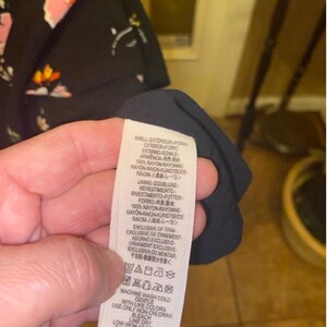 May include: A black and white care label with instructions for washing and caring for a garment. The label says "Machine wash cold with like colours, gentle, use only non-chlorine bleach, low iron as needed, line dry, do not dry clean."