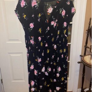 May include: A black midi dress with a floral print featuring pink, yellow, and green flowers. The dress has a V-neckline and short sleeves.