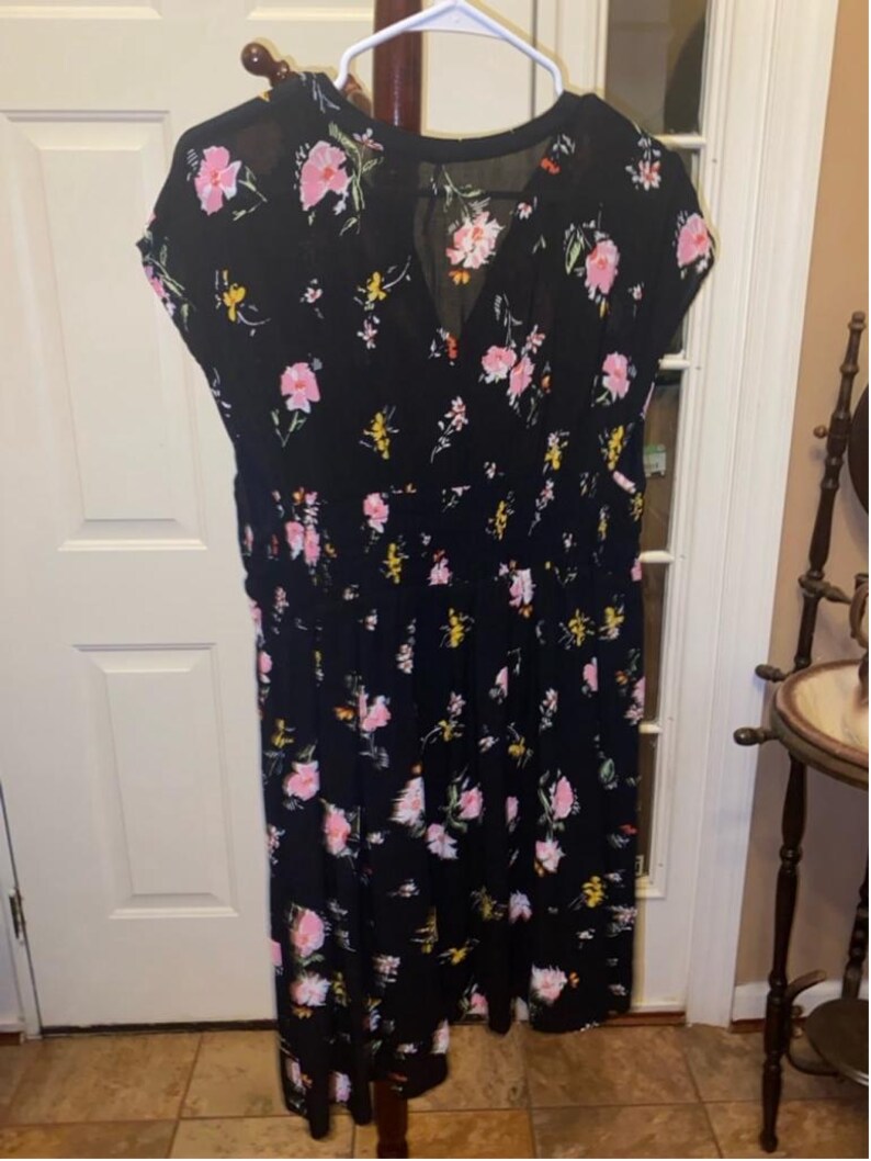 May include: A black midi dress with a floral print featuring pink, yellow, and green flowers. The dress has a V-neckline and short sleeves.