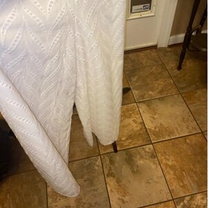 May include: White eyelet fabric with a chevron pattern. The fabric is hanging over a tiled floor.