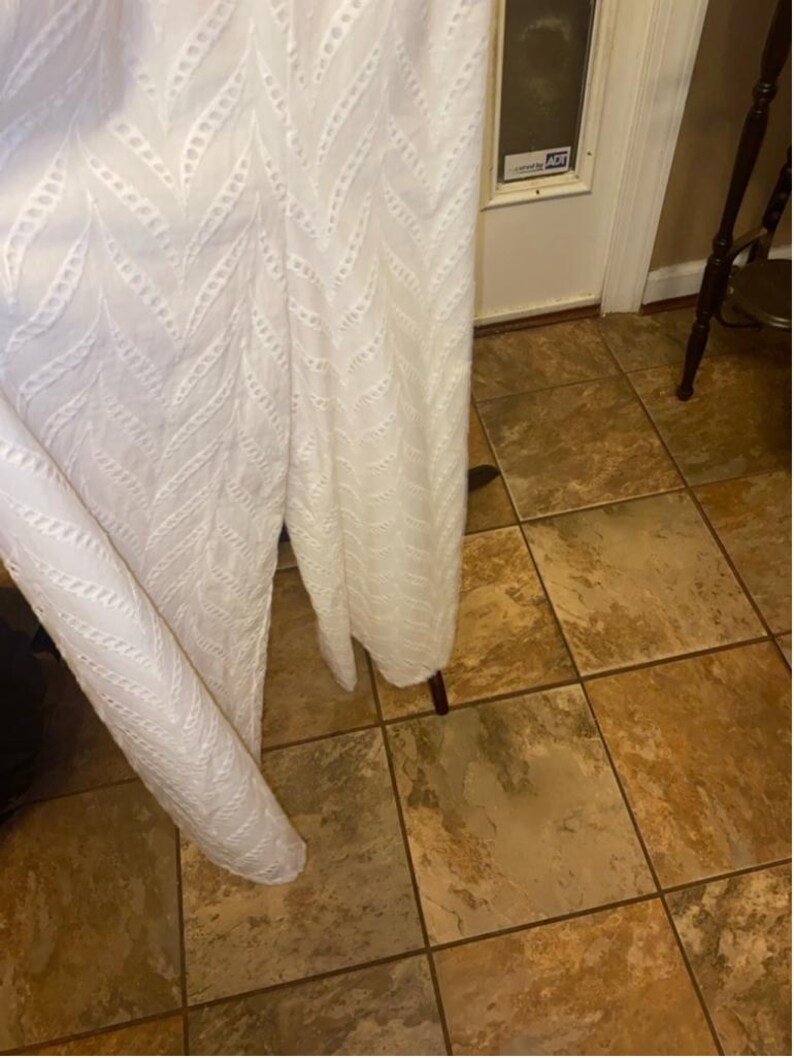 May include: White eyelet fabric with a chevron pattern. The fabric is hanging over a tiled floor.