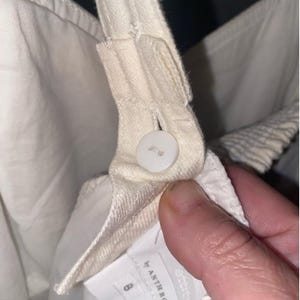 May include: White cotton overalls with a button closure and a label that reads "Anthropologie" and "Made in Indonesia".