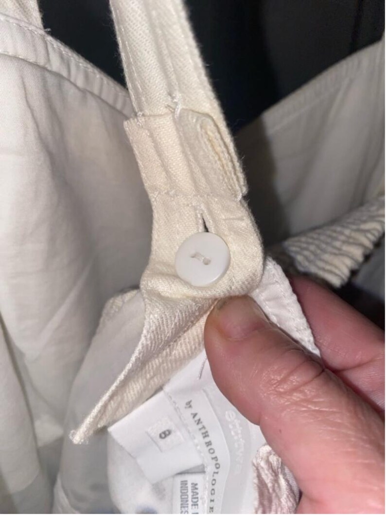May include: White cotton overalls with a button closure and a label that reads "Anthropologie" and "Made in Indonesia".
