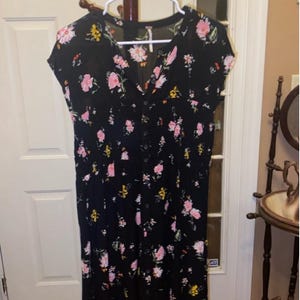 May include: A black midi dress with a floral print featuring pink, yellow, and white flowers. The dress has a V-neckline and short sleeves.