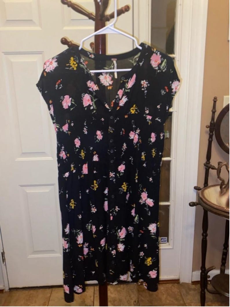 May include: A black midi dress with a floral print featuring pink, yellow, and white flowers. The dress has a V-neckline and short sleeves.