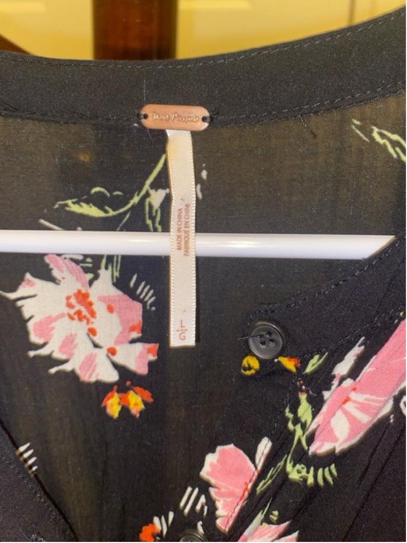 May include: Black floral dress with a button fastening and a Free People label. The dress features a large floral print with pink, white and green flowers on a black background. The label reads "Free People" and "Made in Indonesia".