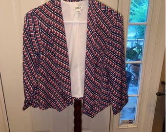 May include: A patterned blazer in red, white, and navy blue hangs on a wooden coat rack. The blazer has a geometric design and a white interior lining. The tag reads "Cato".