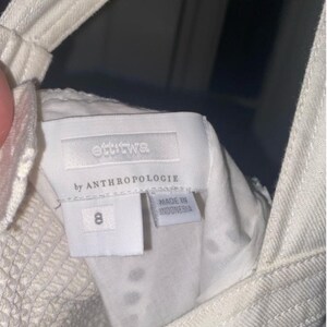 May include: White denim overalls with a white tag that reads "ettika by Anthropologie" and "Made in Indonesia". The tag also has the number "8" on it.