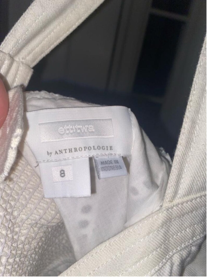 May include: White denim overalls with a white tag that reads "ettika by Anthropologie" and "Made in Indonesia". The tag also has the number "8" on it.