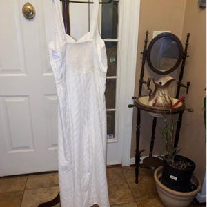 May include: White eyelet maxi dress with a sweetheart neckline and spaghetti straps. The dress is hanging on a wooden hanger.