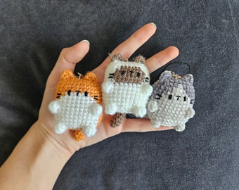 Puede incluir: Tres peluches de gato de crochet en diferentes colores: naranja, marrón y gris. Cada peluche tiene una cara blanca con ojos negros y una nariz rosa.