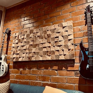 Może przedstawiać: Ściana studia akustycznego z drewnianym geometrycznym dziełem sztuki i dwiema gitarami elektrycznymi. Gitary są białe i czarne, zamontowane na czerwonej ceglanej ścianie. Drewniane dzieło sztuki składa się z małych, kątowych drewnianych bloków.