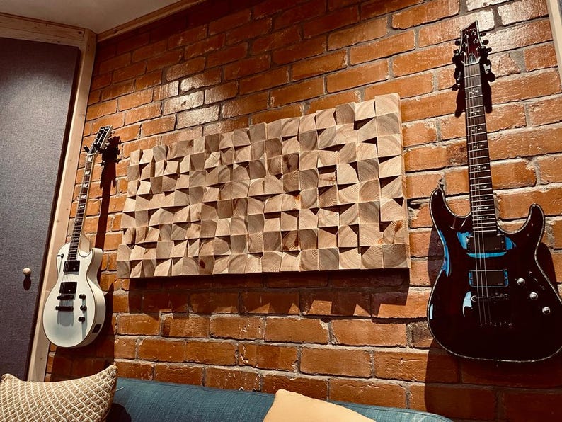 Op de afbeelding: Akoestische studio muur met een geometrisch houten kunstwerk en twee elektrische gitaren. De gitaren zijn wit en zwart, gemonteerd op een rode bakstenen muur. Het houten kunstwerk is gemaakt van kleine, schuine houten blokken.