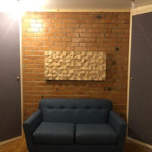 Op de afbeelding: Akoestische behandelkamer met een blauwe bank, een houten geluidsdiffuser en twee geluiddempende panelen. De bakstenen muur voegt een rustieke touch toe aan de geluiddichte ruimte. De kamer is ontworpen voor geluidsopname of muziekpraktijk.