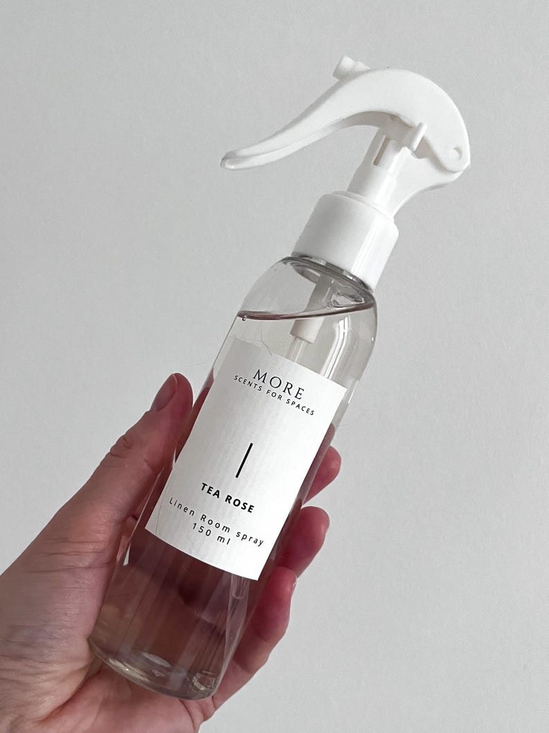 Peut inclure: Une bouteille en verre transparente avec une buse de pulv&eacute;risation blanche remplie d'un liquide rose clair. La bouteille porte une &eacute;tiquette blanche avec le texte "MORE SCENTS FOR SPACES" et "TEA ROSE Linen Room Spray 150 ml".