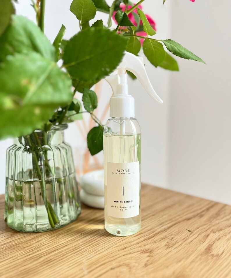 Peut inclure: Une bouteille en verre transparente avec une buse de pulv&eacute;risation blanche remplie d'un liquide jaune clair. La bouteille porte une &eacute;tiquette blanche avec le texte "MORE SCENTS FOR SPACES | WHITE LINEN Linen Room Spray 150 ml".