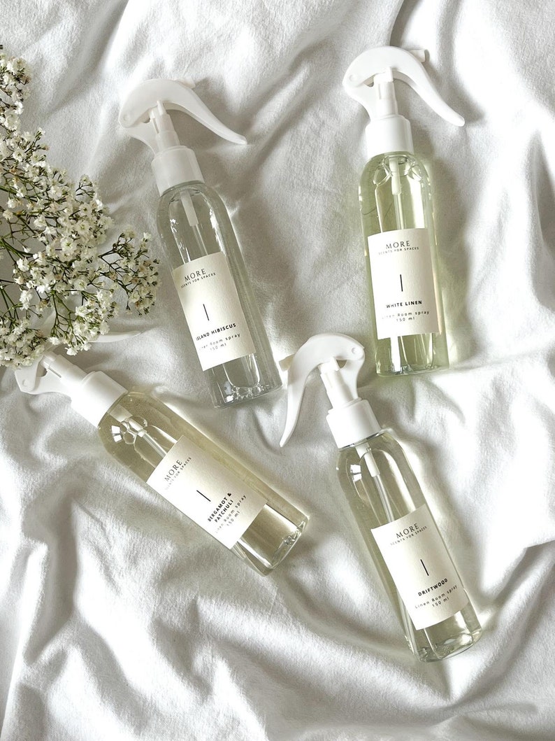 Peut inclure: Quatre flacons pulv&eacute;risateurs en verre transparent avec des embouts pulv&eacute;risateurs blancs et des &eacute;tiquettes. Les &eacute;tiquettes portent le texte "MORE SCENTS FOR SPACES" et les noms des parfums : "Island Hibiscus", "White Linen", "Bergamot & Basil", et "Driftwood".