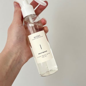 Peut inclure: Un flacon pulv&eacute;risateur en plastique blanc contenant un liquide clair. L'&eacute;tiquette indique "MORE SCENTS FOR SPACES" et "DRIFTWOOD Linen Room Spray 150 ml".