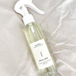 Peut inclure: Une bouteille en verre transparente avec une buse de pulv&eacute;risation blanche remplie d'un liquide clair. La bouteille porte une &eacute;tiquette blanche avec le texte "MORE SCENTS FOR SPACES" et "WHITE LINEN Linen Room Spray 150 ml".