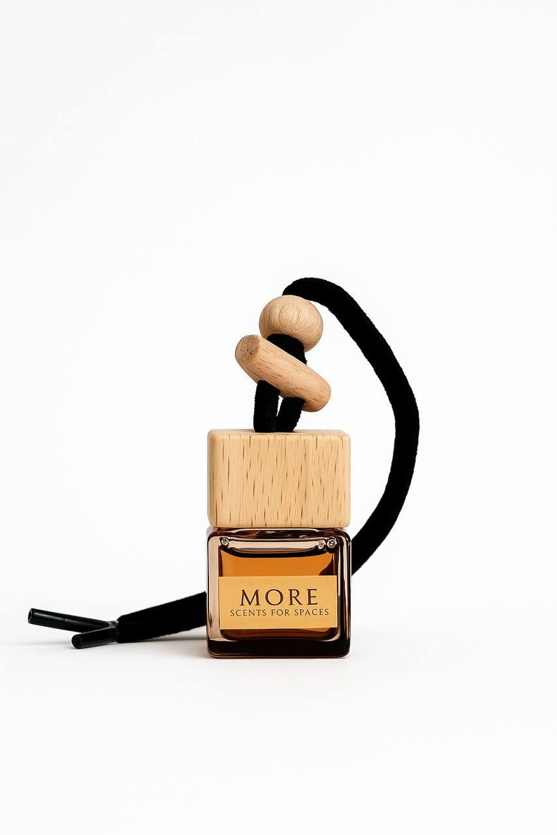 Peut inclure: Petite bouteille carr&eacute;e en verre avec un bouchon en bois et un cordon noir. La bouteille contient un liquide brun clair et porte l'inscription "MORE SCENTS FOR SPACES". Le bouchon en bois est en bois naturel.