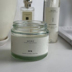 Peut inclure: Un bocal en verre pour bougie avec une &eacute;tiquette blanche sur laquelle est inscrit "MORE SCENTS FOR SPACES ZEN VEGAN & HAND CRAFTED".