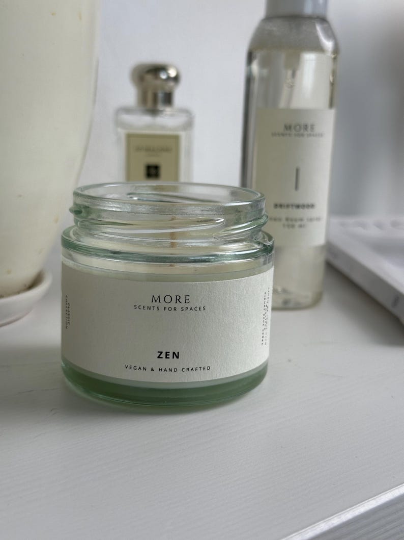 Peut inclure: Un bocal en verre pour bougie avec une &eacute;tiquette blanche sur laquelle est inscrit "MORE SCENTS FOR SPACES ZEN VEGAN & HAND CRAFTED".