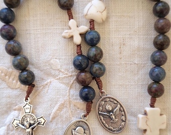 May include: A brown and blue stone rosary with a silver crucifix, a silver chalice pendant, a silver dove pendant, and two white stone cross charms.