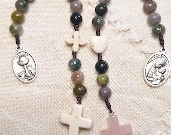 May include: A green, brown, and gray stone rosary with a white cross, a white heart, and two silver medallions. One medallion features a chalice and the other features a mother and child.