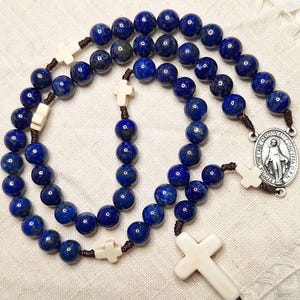 Peut inclure: Un chapelet en lapis-lazuli bleu avec des perles en os blanc et un pendentif en argent de la médaille miraculeuse. La médaille représente une image de la Vierge Marie et le texte "ORIGINAL MIRACULOUS MEDAL CONCEPCION DE P.I."