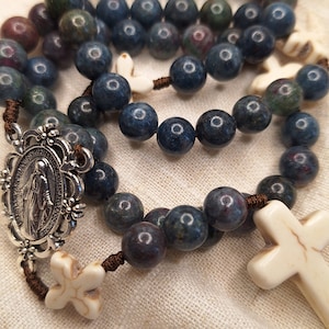 Peut inclure: Un chapelet bleu et blanc avec un pendentif en argent représentant la Vierge Marie. Les perles du chapelet sont en pierre bleue avec des accents blancs. Le pendentif est entouré d'un motif floral en argent.