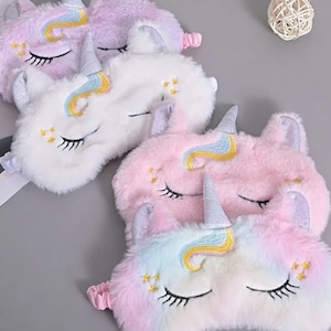 May include: Three plush unicorn eye masks in pink, white, and rainbow colors. Each mask has a gold horn, embroidered eyes, and gold stars.
