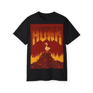 Pode incluir: Camiseta preta com um gráfico de um ganso branco em pé sobre uma pilha de ossos com chamas ao redor. O texto "HONK" está acima do ganso em uma fonte amarela e laranja.