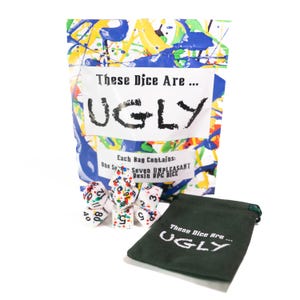 May include: A set of seven colorful dice in a white bag with the text "These Dice Are... UGLY" printed on it. The dice are white with colorful dots and numbers. The bag is sitting on a white surface next to a green velvet bag with the same text printed on it.