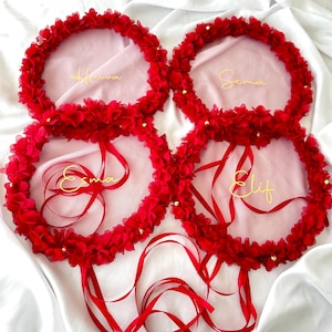 Może przedstawiać: Cztery czerwone wianki kwiatowe z złotymi napisami na białym tle. Wianki są ozdobione małymi złotymi koralikami. Napisy na wiankach brzmią: "Havva", "Sema", "Esma" i "Elif".