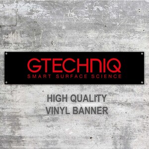Puede incluir: Bandera de vinilo negra con el texto rojo "GTECHNIQ SMART SURFACE SCIENCE". La bandera es rectangular y está montada en una pared gris texturizada. Debajo del texto principal está el texto "HIGH QUALITY VINYL BANNER".