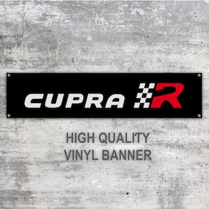 May include: A black vinyl banner with the word "CUPRA" in white block letters, a checkered flag design, and a red "R". The banner also includes the text "HIGH QUALITY VINYL BANNER".