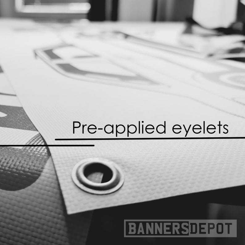 May include: Close-up of a banner with pre-applied eyelets. The banner is white with a textured surface and a metal eyelet. The text "Pre-applied eyelets" is printed on the banner. The Banners Depot logo is visible at the bottom.