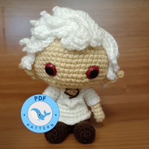 Può includere: Bambola amigurumi all'uncinetto con capelli bianchi, pelle beige e occhi rossi. La bambola indossa una camicia bianca e pantaloni marroni. La bambola è seduta su una superficie di legno. L'immagine include un cerchio blu con il testo "PDF PATTERN" e una balena bianca all'interno.