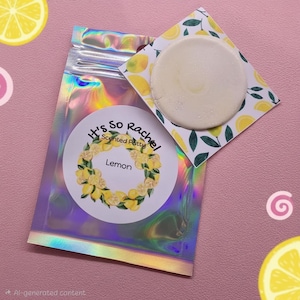 May include: A holographic pouch containing scented putty with a circular label reading It's So Rachel Scented Putty Lemon, featuring a lemon wreath illustration. A circular white putty disc sits on a square card with a lemon and leaf pattern.