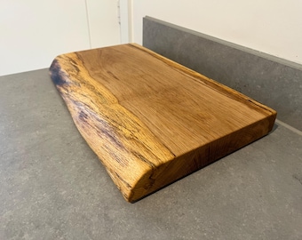May include: A large, natural wood cutting board with a live edge and a smooth, polished surface. The board is made from a single piece of wood and has a natural, rustic look.