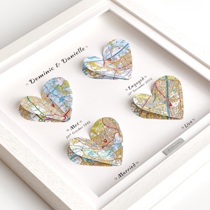 Pode incluir: Uma peça de arte de parede com moldura branca apresentando quatro corações de papel em camadas feitos de mapas coloridos. O texto diz Dominic & Danielle, Met 10th October 1992, Engaged 31st December 2002, Married e Live, com uma placa prateada.
