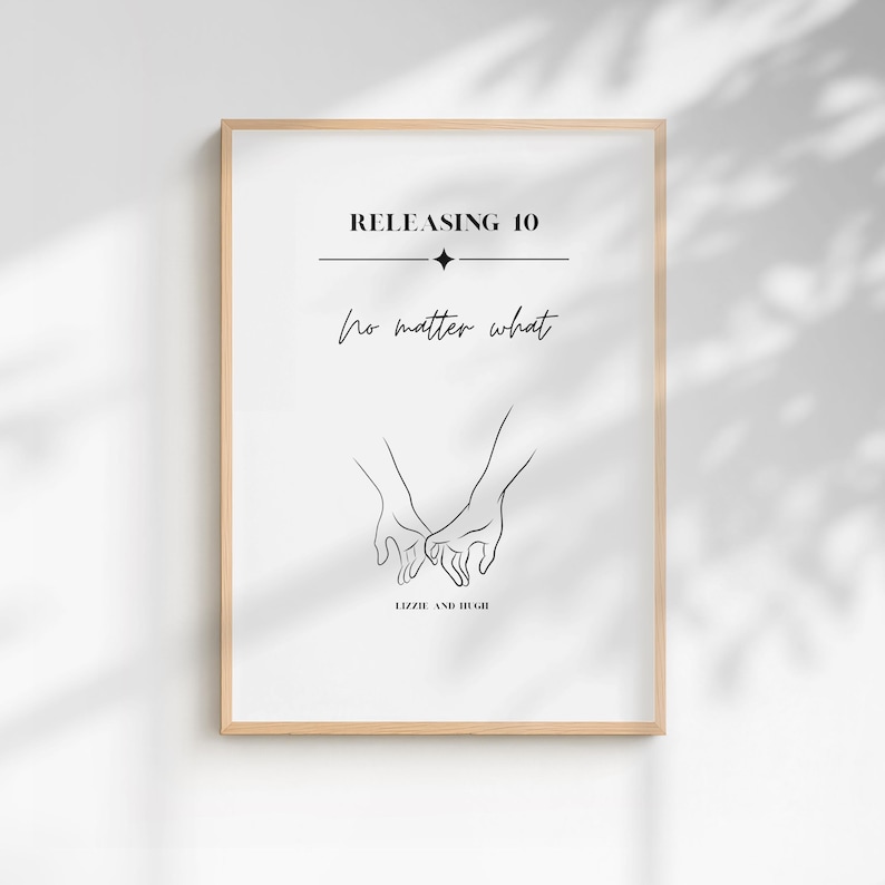 May include: A framed wall art print featuring a minimalist black line drawing of two hands holding each other. The text reads RELEASING 10, no matter what, and LIZZIE AND HUGH. The design is centered on a white background within a light wood frame.