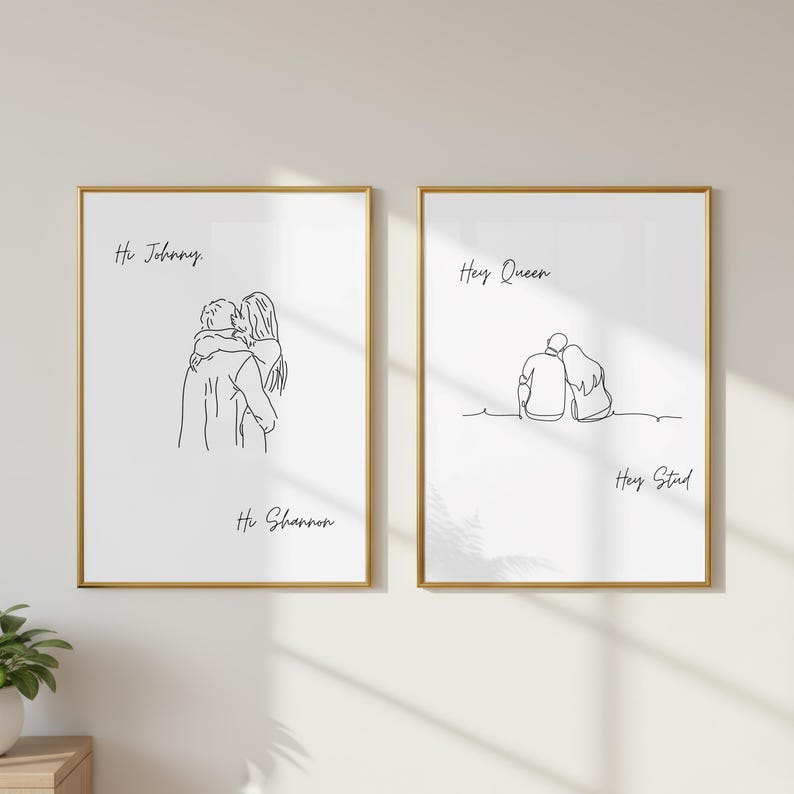 May include: Two framed wall art prints with gold borders featuring black line art illustrations of couples. The left print shows a couple embracing with the text Hi Johnny and Hi Shannon. The right print shows a couple sitting with the text Hey Queen and Hey Stud.