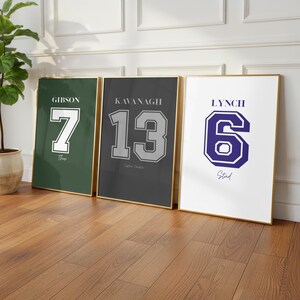 May include: Three framed prints with gold borders, each featuring a jersey-style design. The prints display the names Gibson, Kavanagh, and Lynch, along with the numbers 7, 13, and 6, respectively. The color schemes are green, gray, and white.