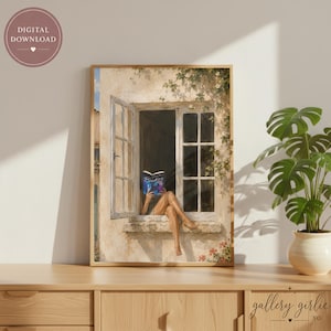 May include: A framed wall art print depicting a person sitting on a stone window ledge reading a book. The scene features a cream-colored building exterior with an open window, green climbing vines, and a blue book cover with the text Reading.