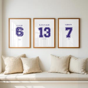 May include: Three framed wall art prints with wooden frames. Each print features a name, a large jersey-style number in dark blue, and a smaller script name below. The prints display the names Lynch 6, Kavanagh 13, and Gibson 7.